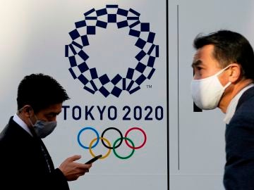 Dos personas pasean con el logo de los Juegos Olímpicos de Tokio 2020 de fondo.